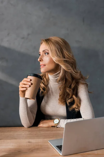 Attractive businesswoman sitting at table and holding paper cup — Stock Photo