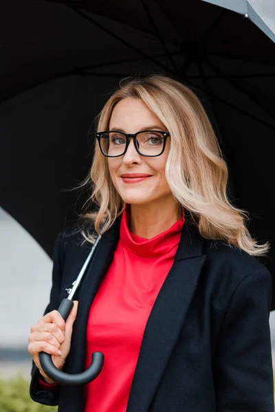 Attractive businesswoman in coat and glasses holding black umbrella — Stock Photo