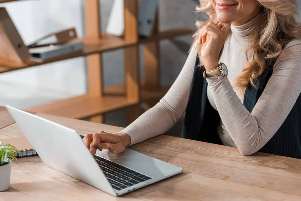 Cropped view of businesswoman sitting at table and using laptop — Stock Photo
