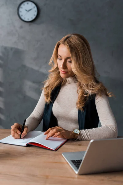 Mulher de negócios atraente sentado à mesa e escrevendo em notebook — Fotografia de Stock