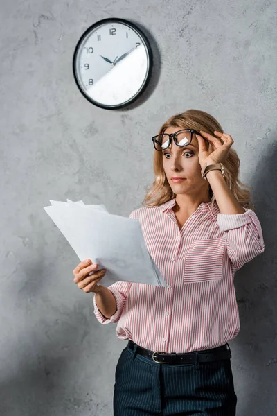 Приваблива і шокована бізнес-леді в окулярах дивиться на папери — стокове фото