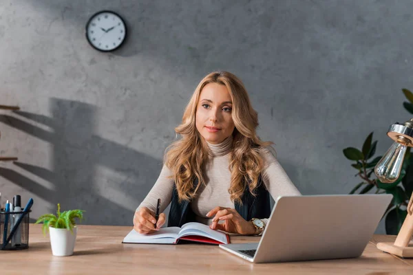 Attractive and dreamy businesswoman sitting at table and holding pen — Stock Photo