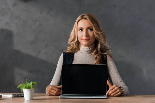 Attraktive und blonde Geschäftsfrau sitzt mit Laptop am Tisch — Stockfoto