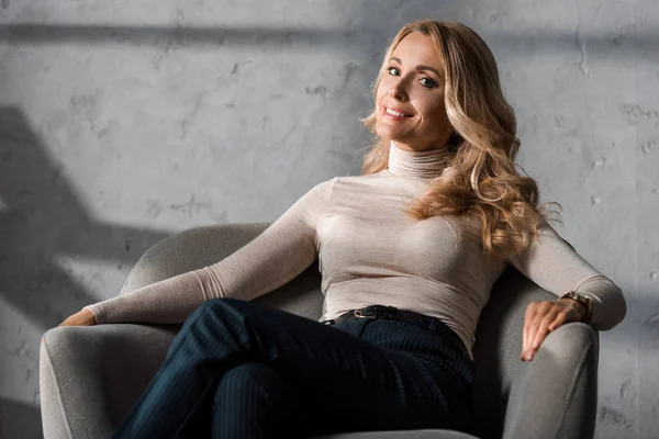Attractive and blonde businesswoman smiling and sitting on armchair — Stock Photo