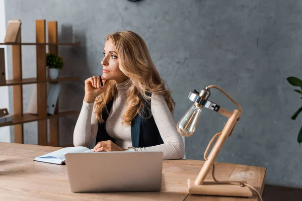 Attraktive und verträumte Geschäftsfrau, die am Tisch sitzt und Stift in der Hand hält — Stockfoto