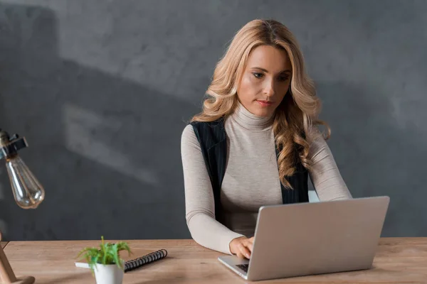 Mulher de negócios atraente e loira sentada à mesa e usando laptop — Fotografia de Stock