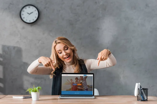 KYIV, UCRAINA - 16 AGOSTO 2019: donna d'affari sorridente che punta con le dita sul sito web di couchsurfing per laptop — Foto stock