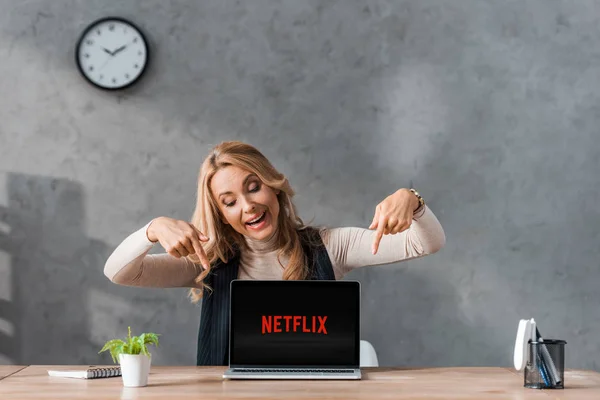 KYIV, UCRAINA - 16 AGOSTO 2019: donna d'affari sorridente che punta con le dita il computer portatile con logo netflix — Foto stock