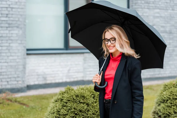 Atractiva y sonriente empresaria con abrigo negro sosteniendo paraguas — Stock Photo