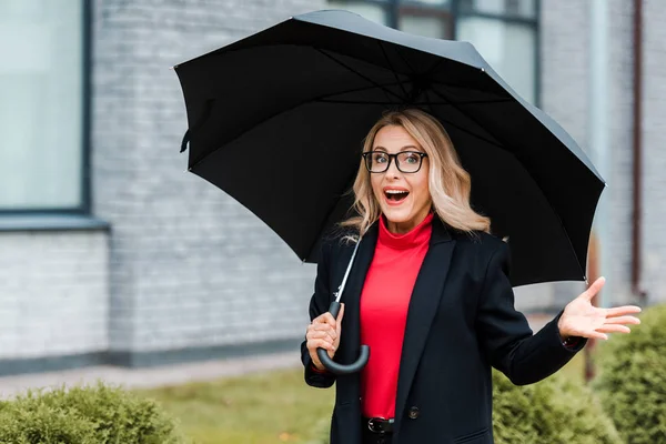 Привлекательная и шокированная деловая женщина в черном пальто с зонтиком — стоковое фото