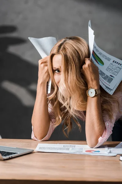 Attractive and sad businesswoman holding papers and looking at camera in office — Stock Photo