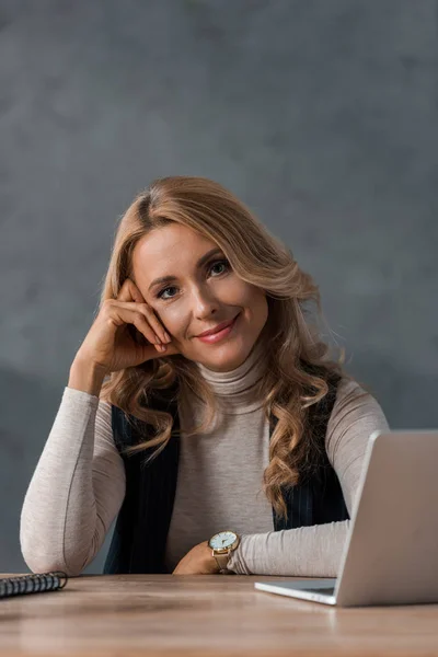 Attraktive und blonde Geschäftsfrau, die am Tisch sitzt und in die Kamera schaut — Stockfoto