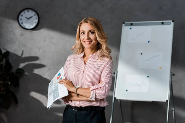 Attractive and blonde businesswoman in shirt smiling and holding papers — Stock Photo