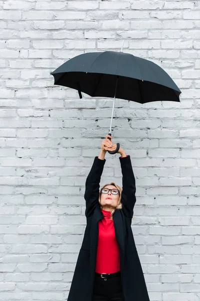 Atractiva y rubia empresaria con abrigo negro sosteniendo paraguas - foto de stock