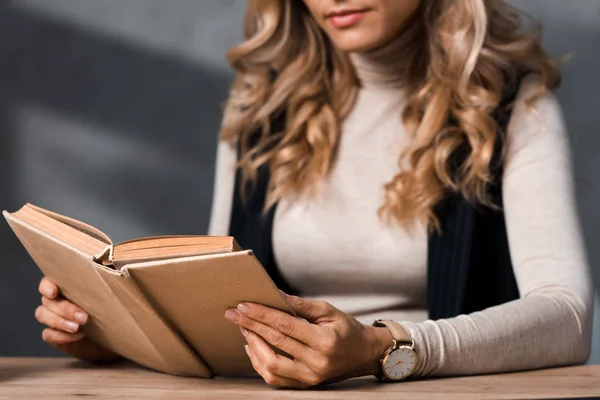 Vista ritagliata di donna d'affari bionda seduta a tavola e libro di lettura in ufficio — Foto stock