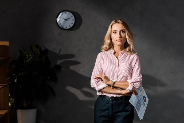 Attractive and blonde businesswoman in shirt holding papers in office — Stock Photo