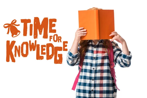 Pupil covering face with orange book near time for knowledge letters on white — Stock Photo