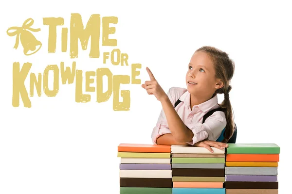 Positive schoolkid pointing with finger at time for knowledge letters near colorful books on white — Stock Photo