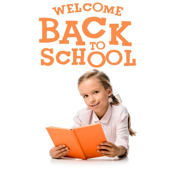 Heureux écolier tenant livre orange et souriant presque bienvenue lettres de retour à l'école sur blanc — Photo de stock