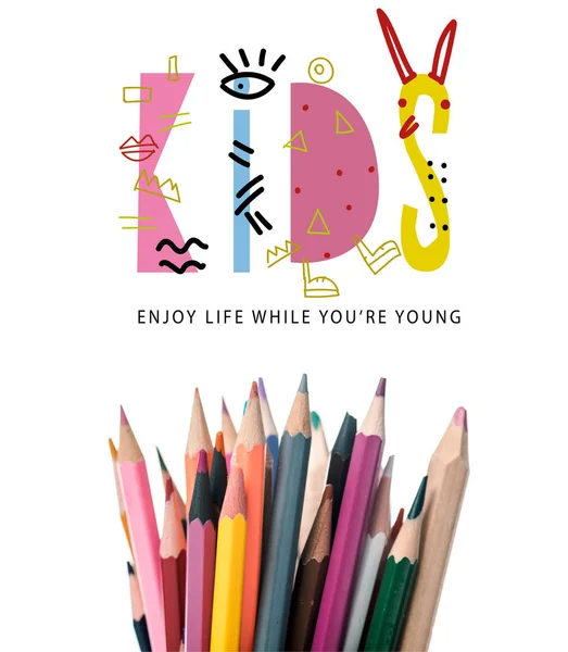 Красочные карандаши рядом с детьми наслаждаться жизнью, пока вы молодые буквы на белом — стоковое фото