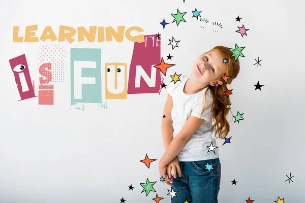 Happy redhead kid looking at camera near learning is fun letters on white — Stock Photo