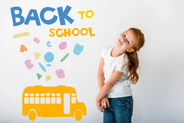 Щаслива руда дитина дивиться на камеру біля автобуса і назад до шкільних листів на білому — стокове фото