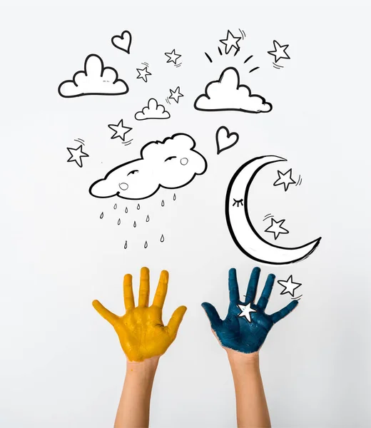 Cropped view of child with blue and yellow paint on hands near moon and stars on white — Stock Photo