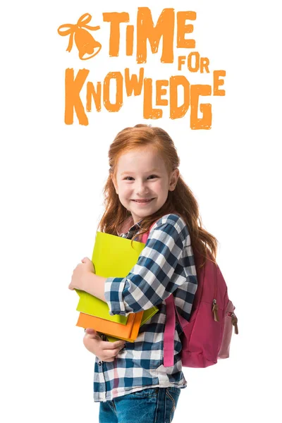 Cheerful redhead pupil holding books near time for knowledge letters isolated on white — Stock Photo