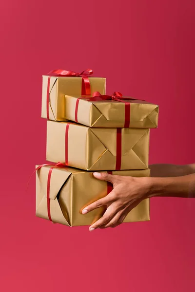 Vista recortada de mujer afroamericana sosteniendo cajas de regalo aisladas en rojo - foto de stock