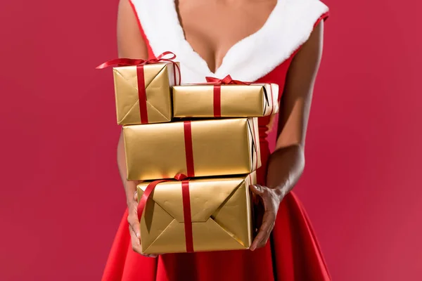 Vue recadrée de fille afro-américaine en chapeau de Père Noël et robe de Noël tenant des boîtes-cadeaux isolés sur rouge — Photo de stock