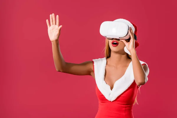 Surprised african american woman in christmas dress standing touching something virtual while using vr headset isolated on red — Stock Photo