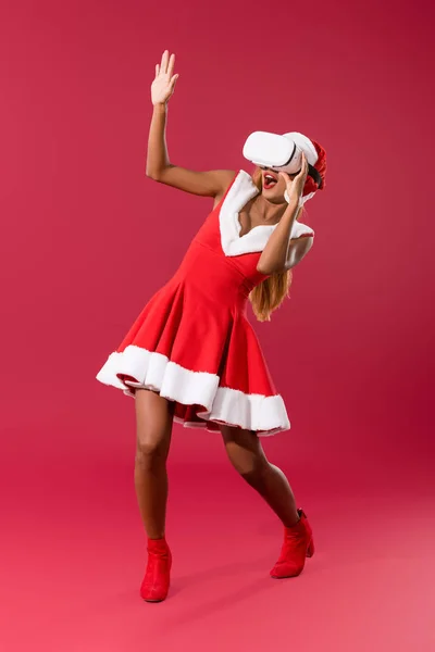 Effrayé afro-américaine fille en robe de Noël gestuelle tout en utilisant vr casque sur fond rouge — Photo de stock