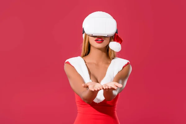 African american girl in christmas dress standing with outstretched hand while using vr headset isolated on red — Stock Photo
