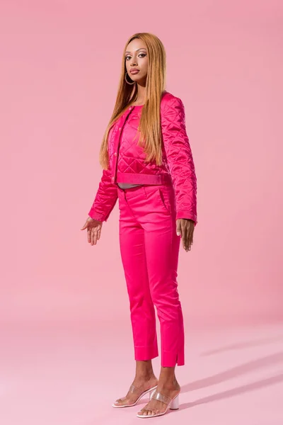 Atractiva, mujer afroamericana de moda de pie sobre fondo rosa, concepto de muñeca de moda - foto de stock