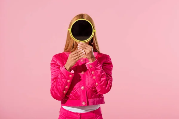 Trendy african american woman hiding face behind mirror isolated on pink, fashion doll concept — Stock Photo