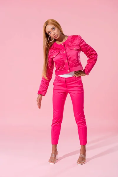 Donna afroamericana alla moda in piedi con mano sull'anca su sfondo rosa, concetto di bambola di moda — Foto stock