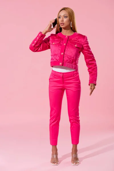Attraente, donna afro-americana alla moda parlando su smartphone su sfondo rosa, concetto di bambola di moda — Foto stock