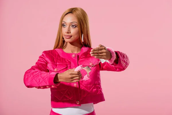 Привлекательная, модная африканская американка в наручниках, отводящая взгляд на розовую, модную куклу — стоковое фото