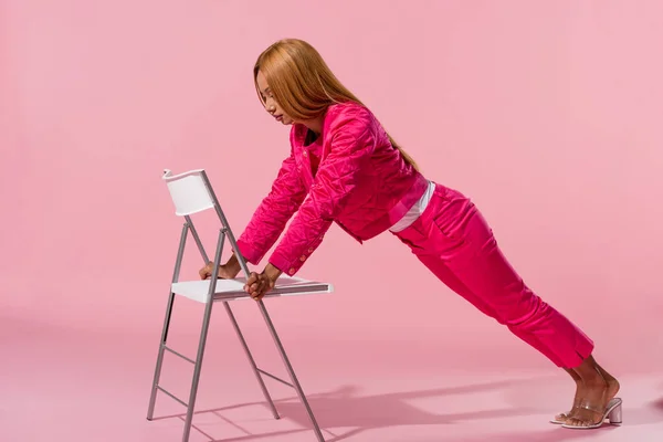 Trendy african american woman leaning on chair on pink background, fashion doll concept — Stock Photo