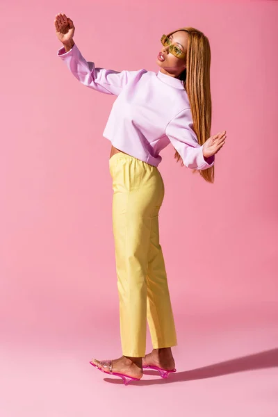 Stylische afrikanisch-amerikanische Frau steht auf rosa Hintergrund, Modepuppenkonzept — Stockfoto