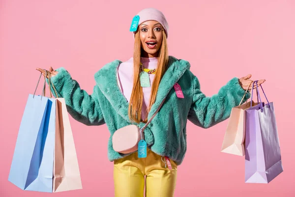 Happy, stylish african american woman holding shopping bags isolated on pink, fashion doll concept — Stock Photo