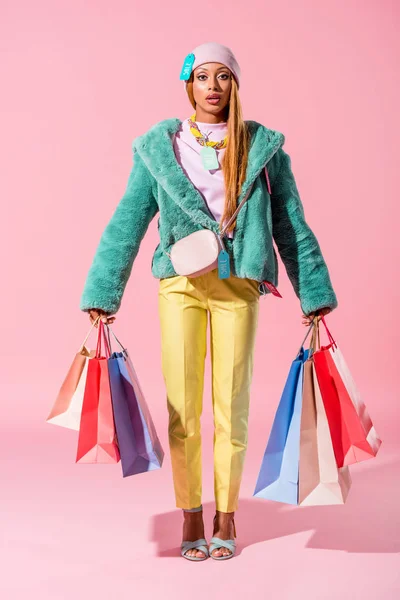 Mujer afroamericana de moda sosteniendo bolsas de compras sobre fondo rosa, concepto de muñeca de moda - foto de stock