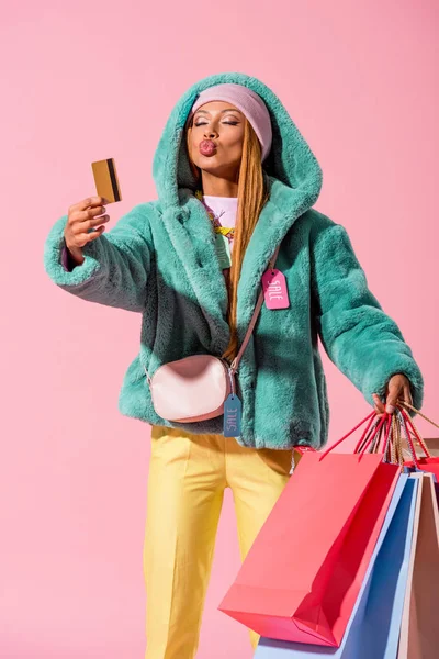 Femme afro-américaine à la mode avec visage de canard tenant carte de crédit et sacs à provisions isolés sur rose, concept de poupée de mode — Photo de stock