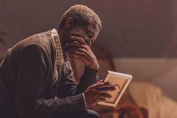 Sênior, homem americano africano deprimido olhando para moldura de fotos — Fotografia de Stock