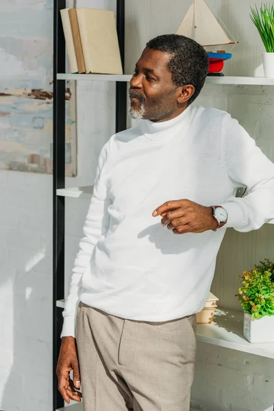 Hombre afroamericano positivo en traje elegante de pie cerca de rack y mirando hacia otro lado - foto de stock