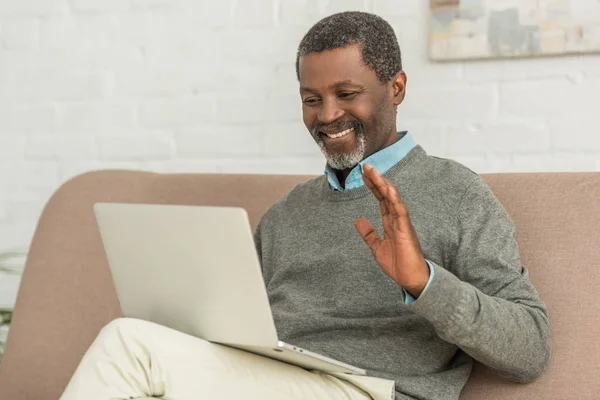 Веселий афроамериканський чоловік махає рукою під час відеодзвінка на ноутбук — стокове фото