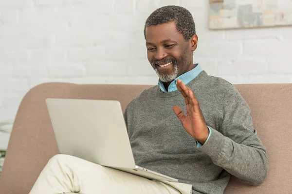 Alegre afro-americano homem acenando mão durante chamada de vídeo no laptop — Fotografia de Stock