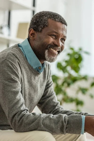 Hombre americano africano alegre en jersey gris sonriendo mientras mira hacia otro lado - foto de stock