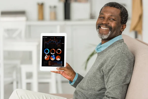Allegro uomo africano americano che tiene tablet digitale con infpografica sullo schermo e sorridente alla fotocamera — Foto stock