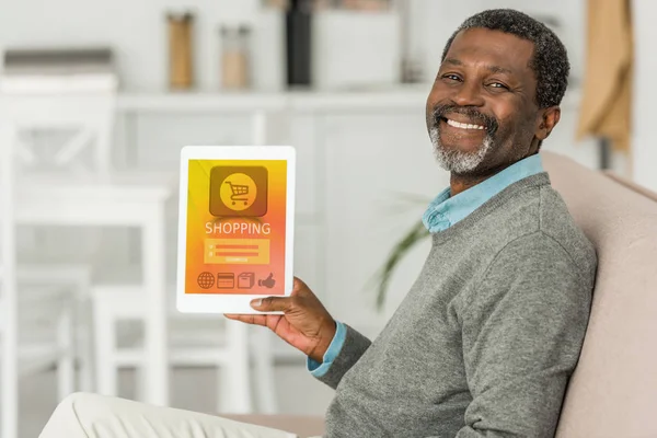 Allegro uomo africano americano con tablet digitale con app di shopping online sullo schermo e sorridente alla fotocamera — Foto stock